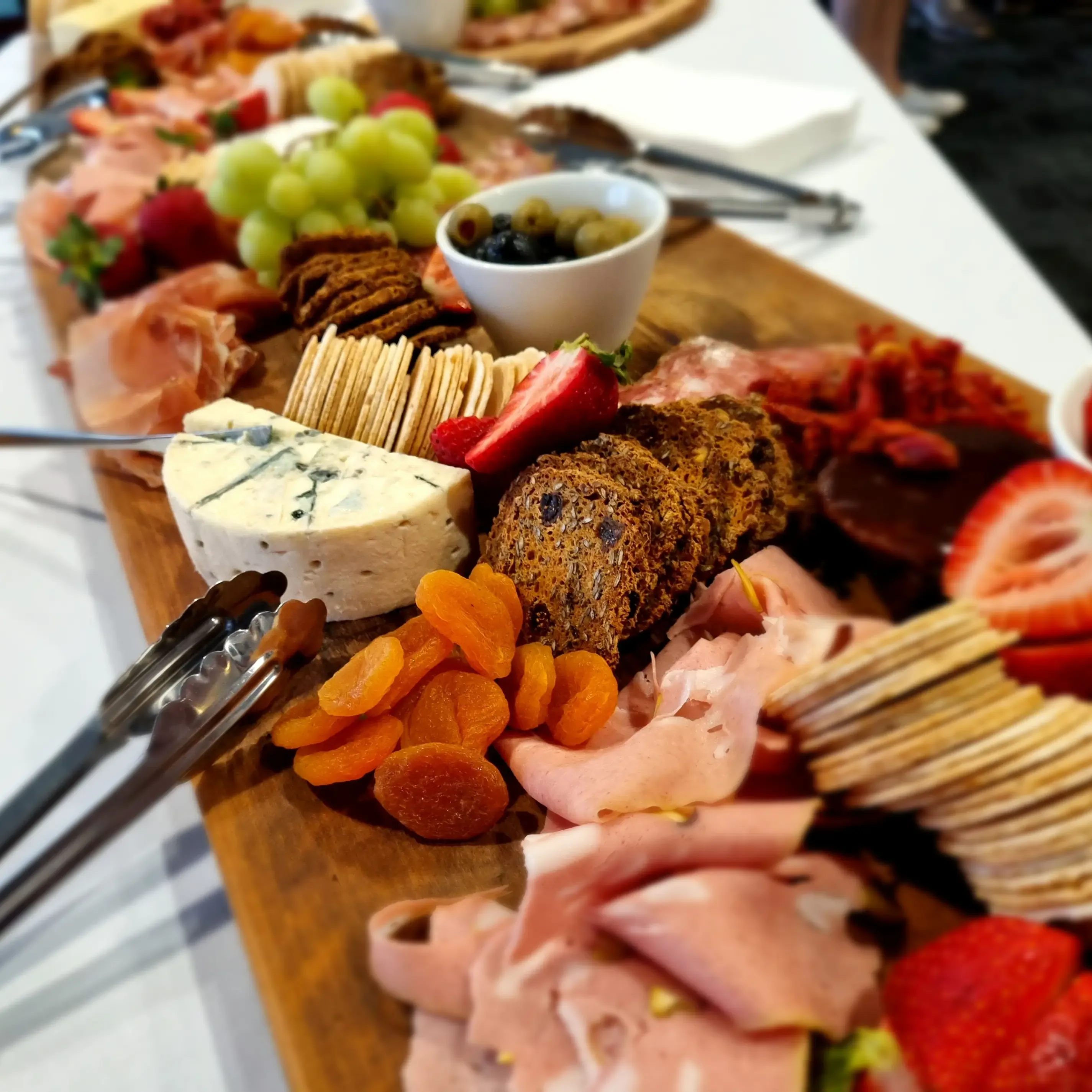 Long grazing table laden with charcuterie, cured meats, cheese and fresh fruit in a rustic barn venue